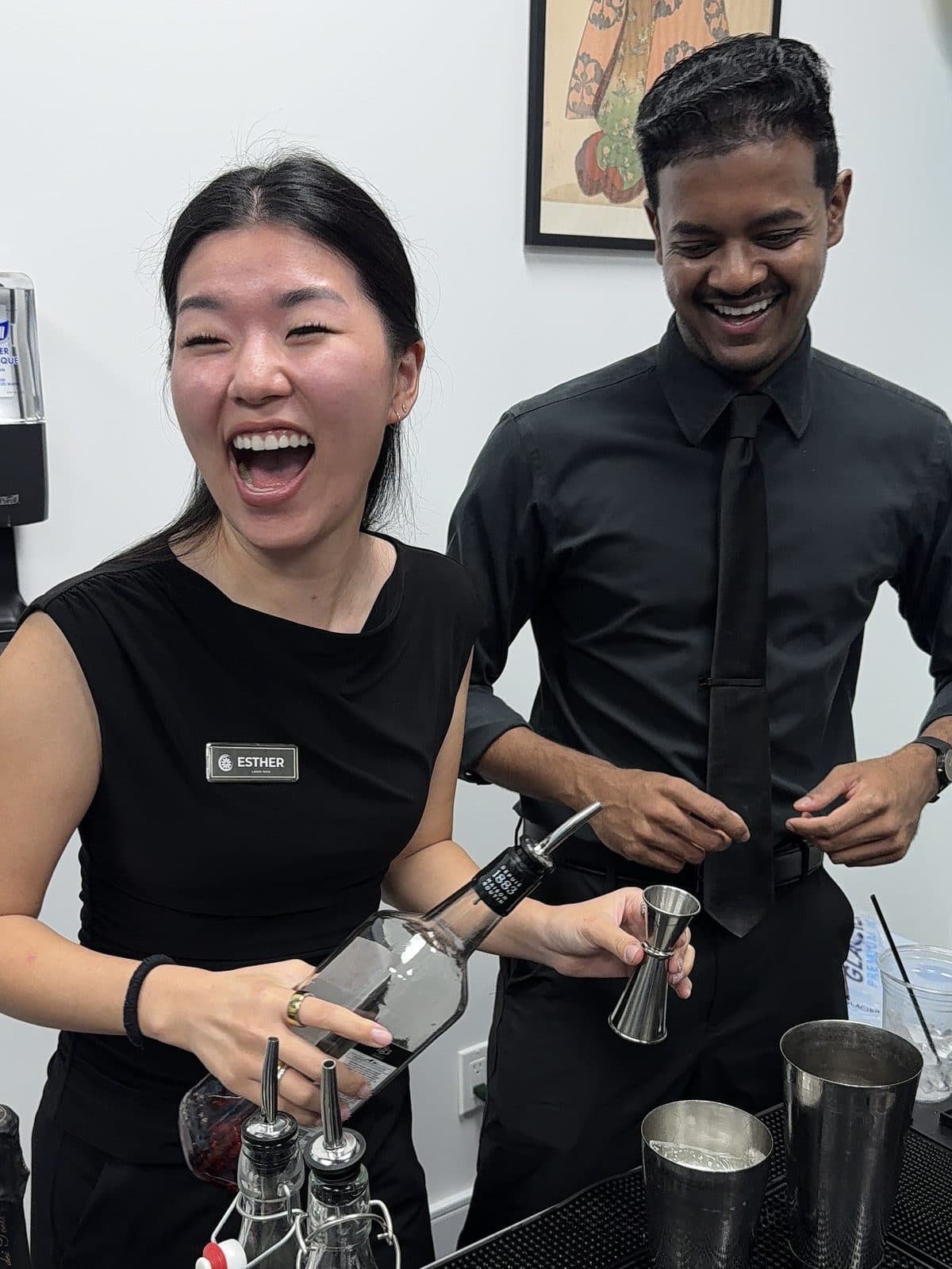 Two people laughing while mixing drinks behind the bar