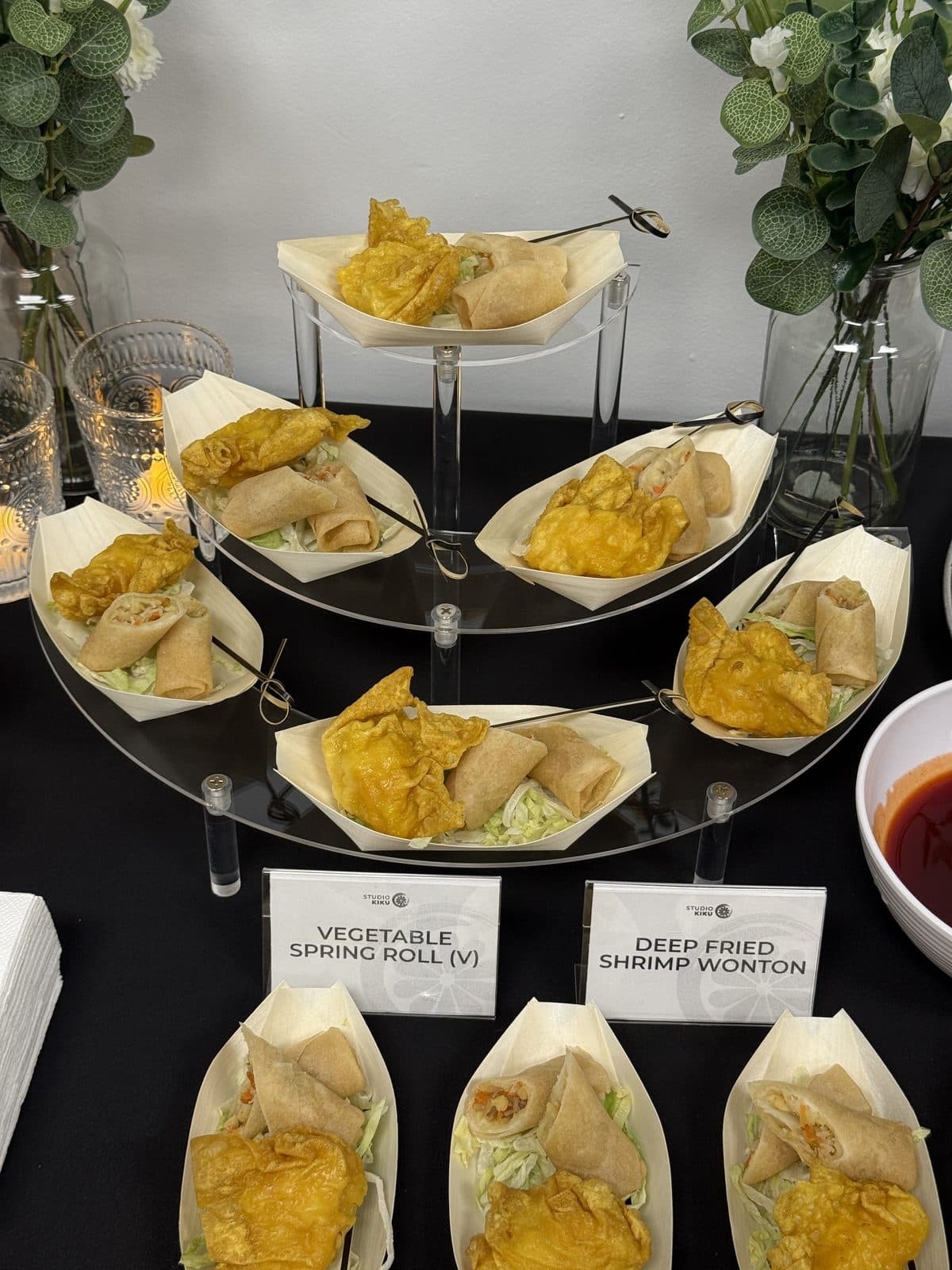 Vegetable spring rolls and deep-fried shrimp wontons in paper boats on a tiered stand