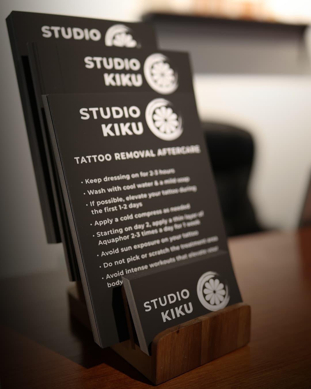 Studio Kiku branded tattoo removal aftercare instruction cards displayed in a wooden stand